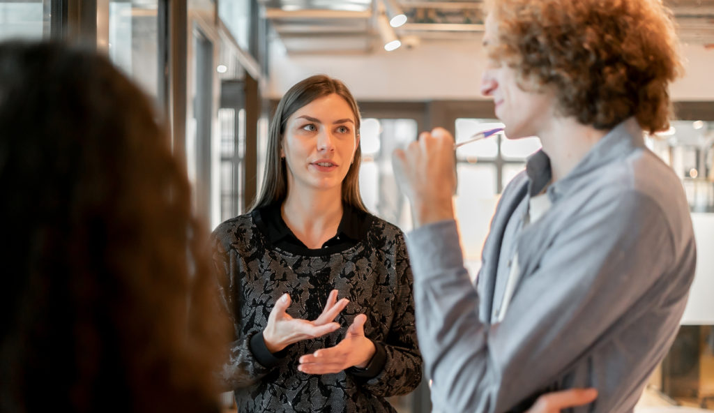 Junge Coworker in einem modernen Büro, die sich in der Nähe einer hellen Fensterfront stehend besprechen © Nuria Segui/Stocksy