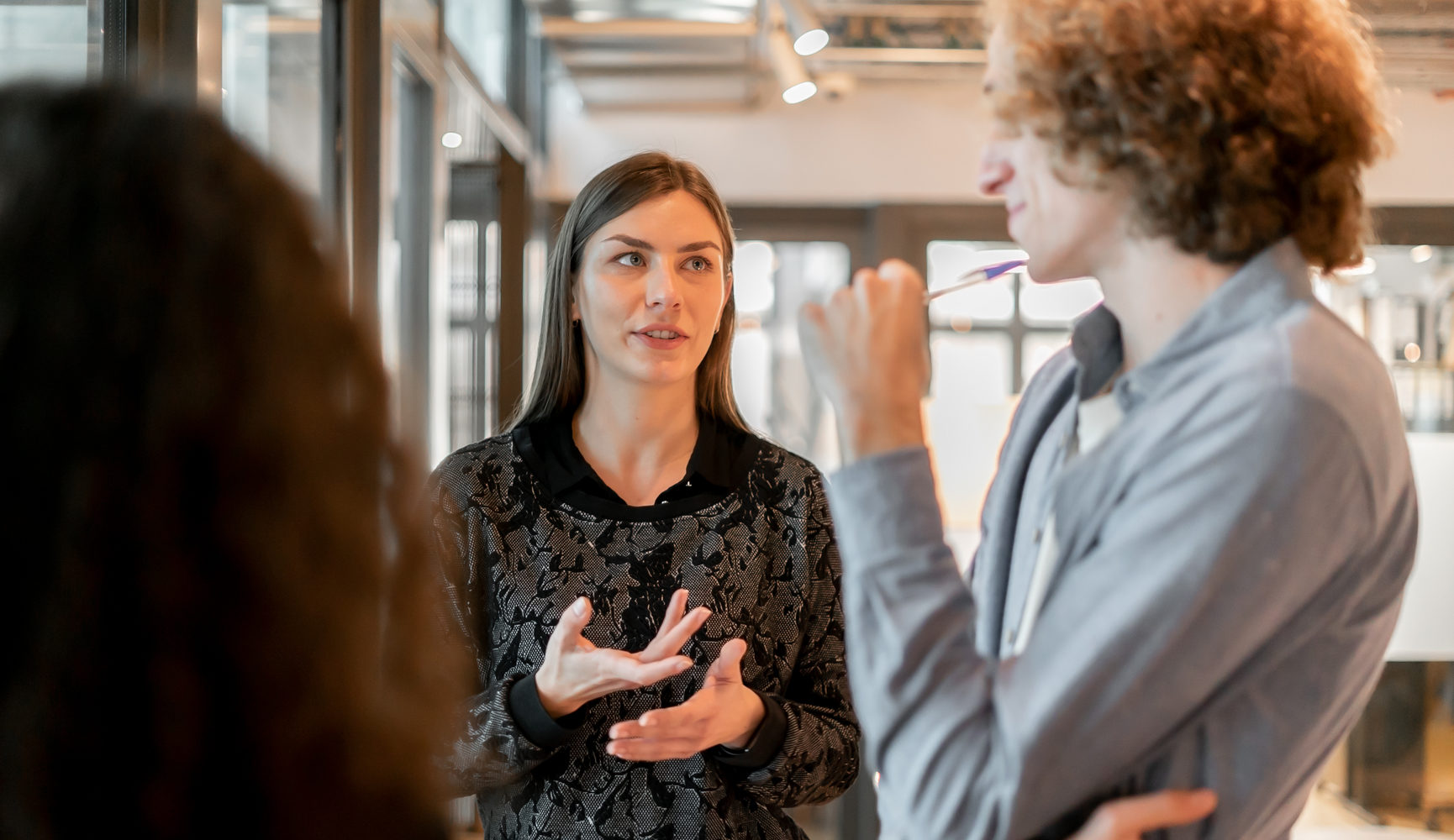 Junge Coworker in einem modernen Büro, die sich in der Nähe einer hellen Fensterfront stehend besprechen © Nuria Segui/Stocksy